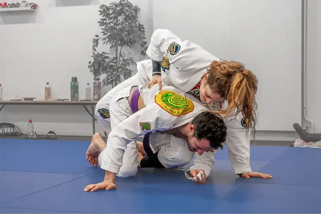 Une pratiquante et un pratiquant en kimono à l'entraînement au sol chez LMNT.